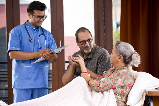 Male Nurse Making A Note Of Senior Patient At Home